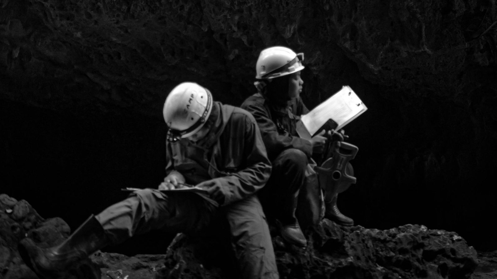 Two mining technicians in hard hats recording survey measurements underground